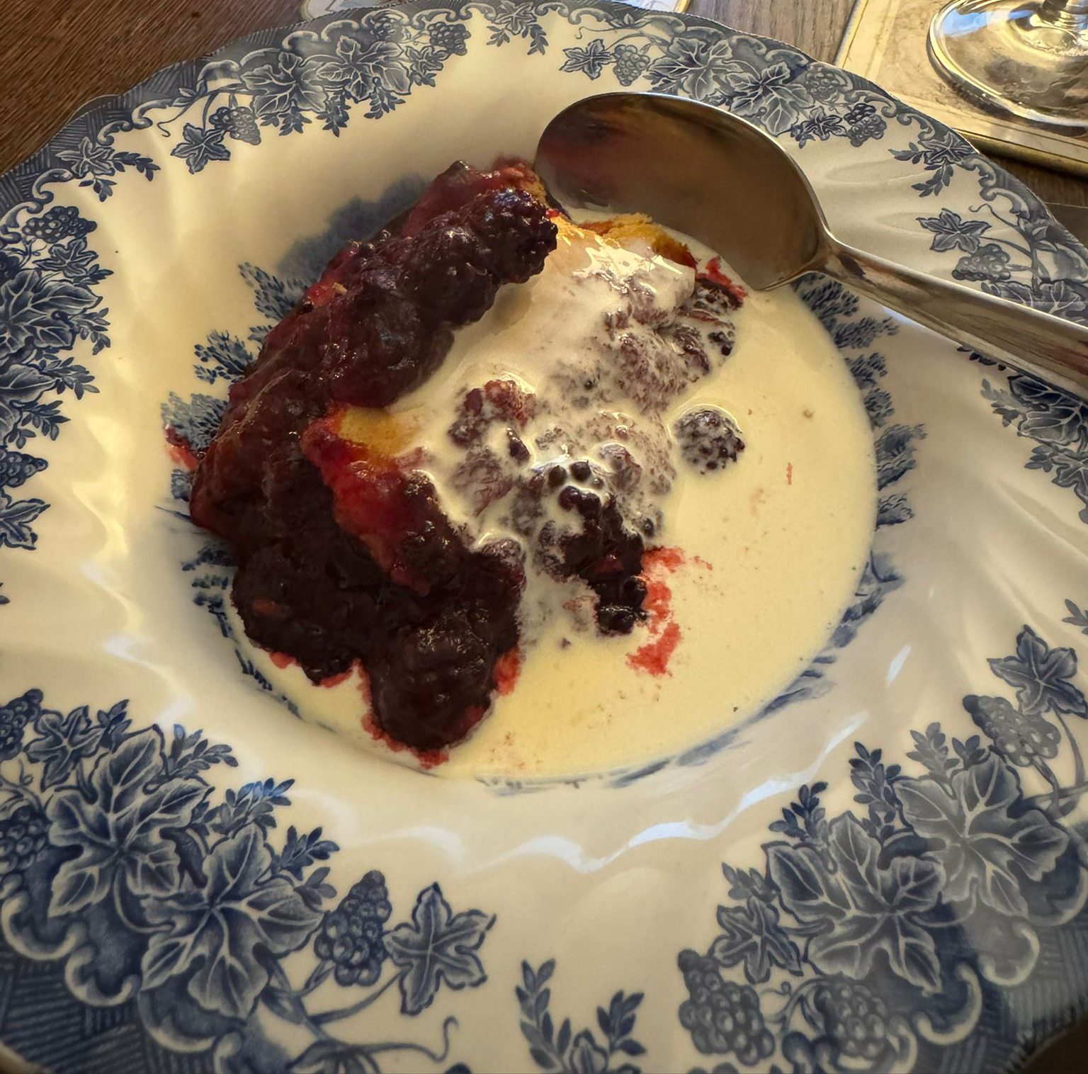 A serving of apple and blackberry pie with fresh cream in a blue-and-white patterned dish