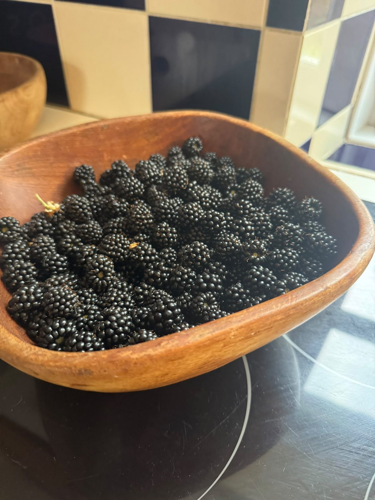A wooden bowl heaped with glossy foraged blackberries on the kitchen worktop