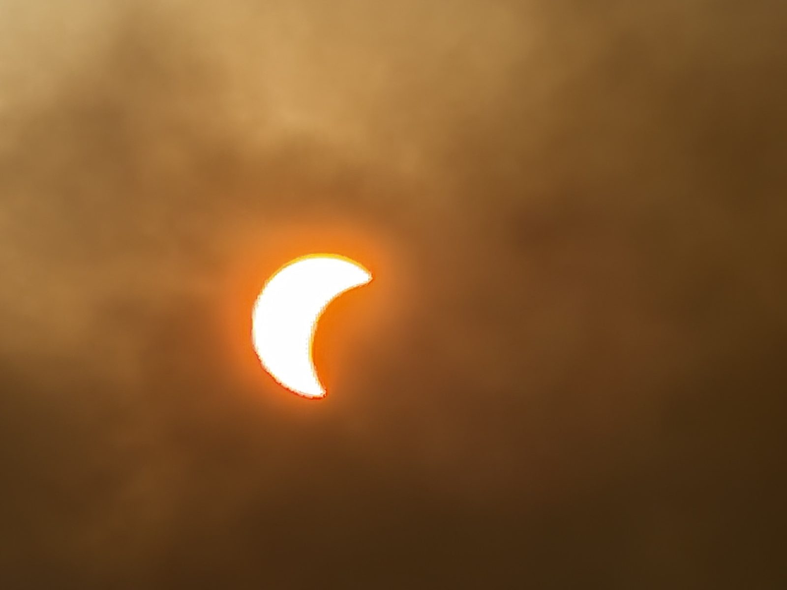 The bright crescent sun during the partial eclipse, softened by smoke