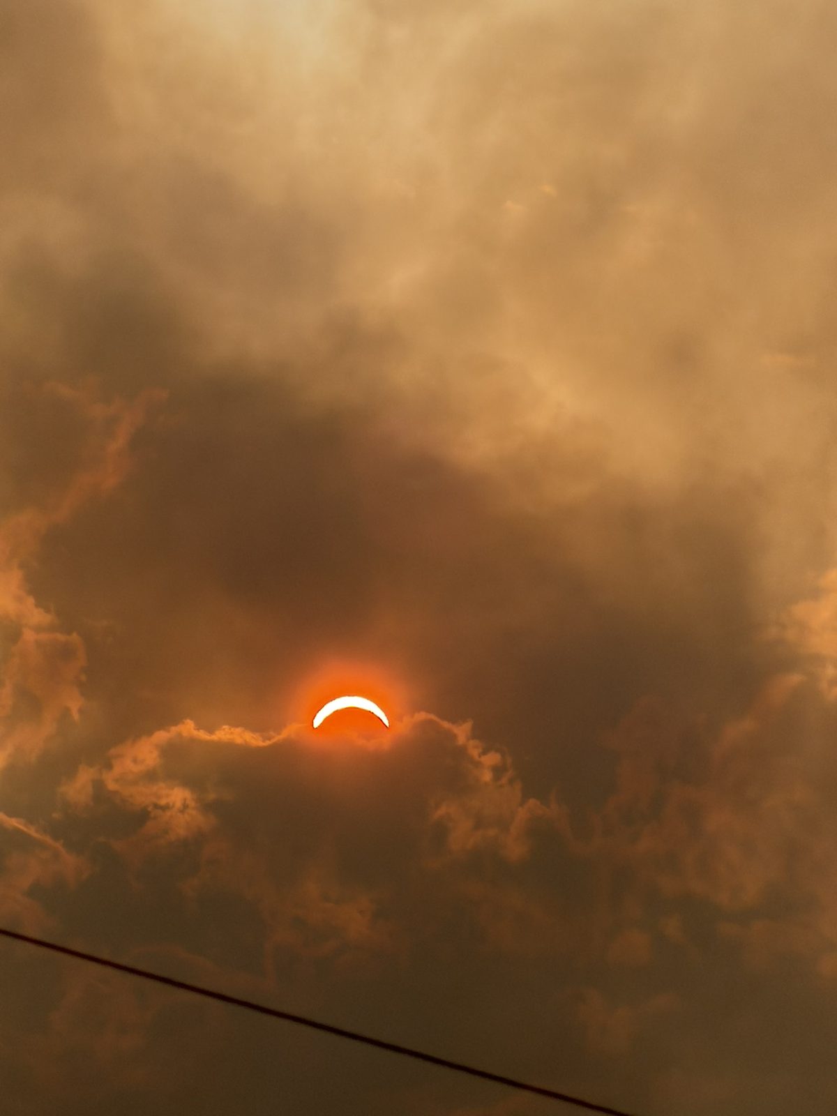 Wide view of the eclipsed sun peeking through heavy smoke-lit clouds over the valley
