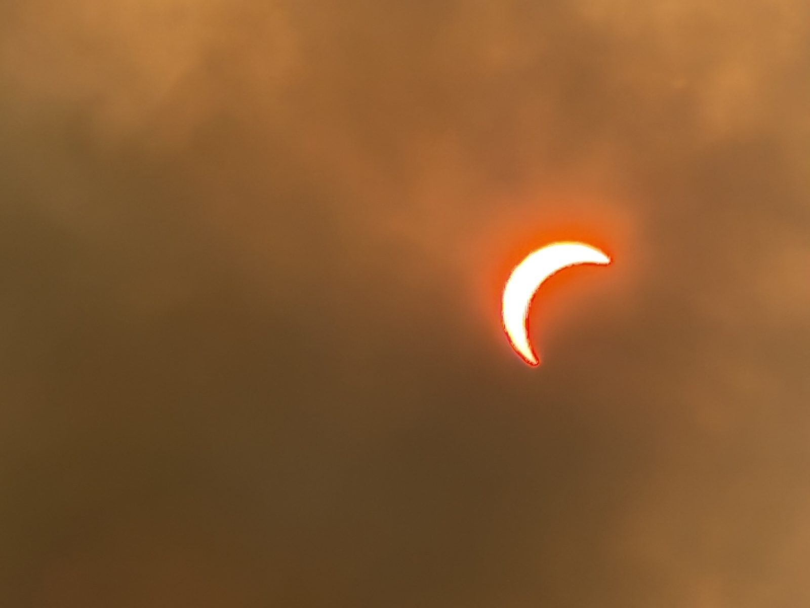 A thin crescent of sun with a red rim, deep in the smoky haze