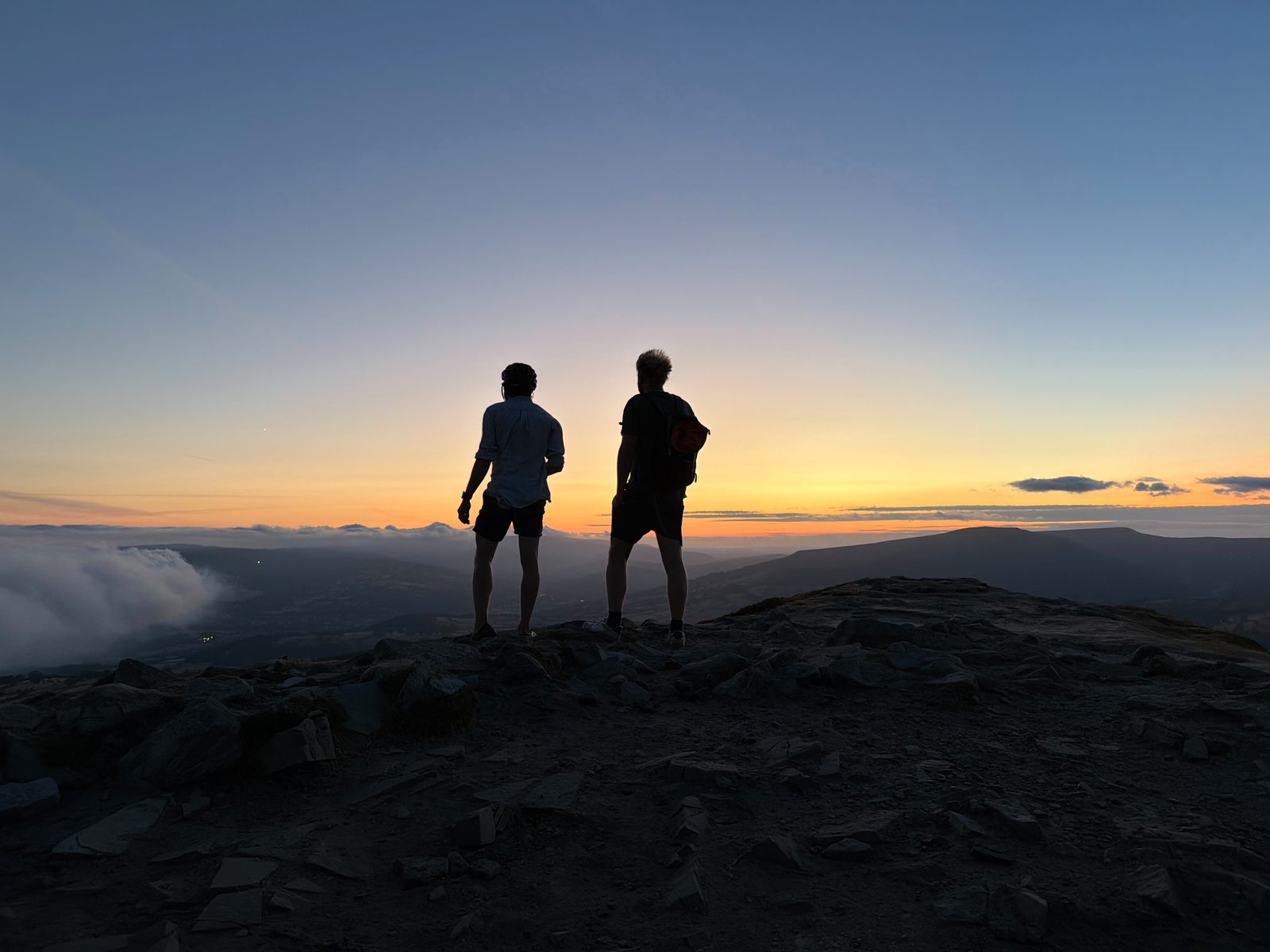 Fred and Ewan silhouetted on the Sugarloaf summit at dusk, watching the wildfire smoke lie among the hills across the valley