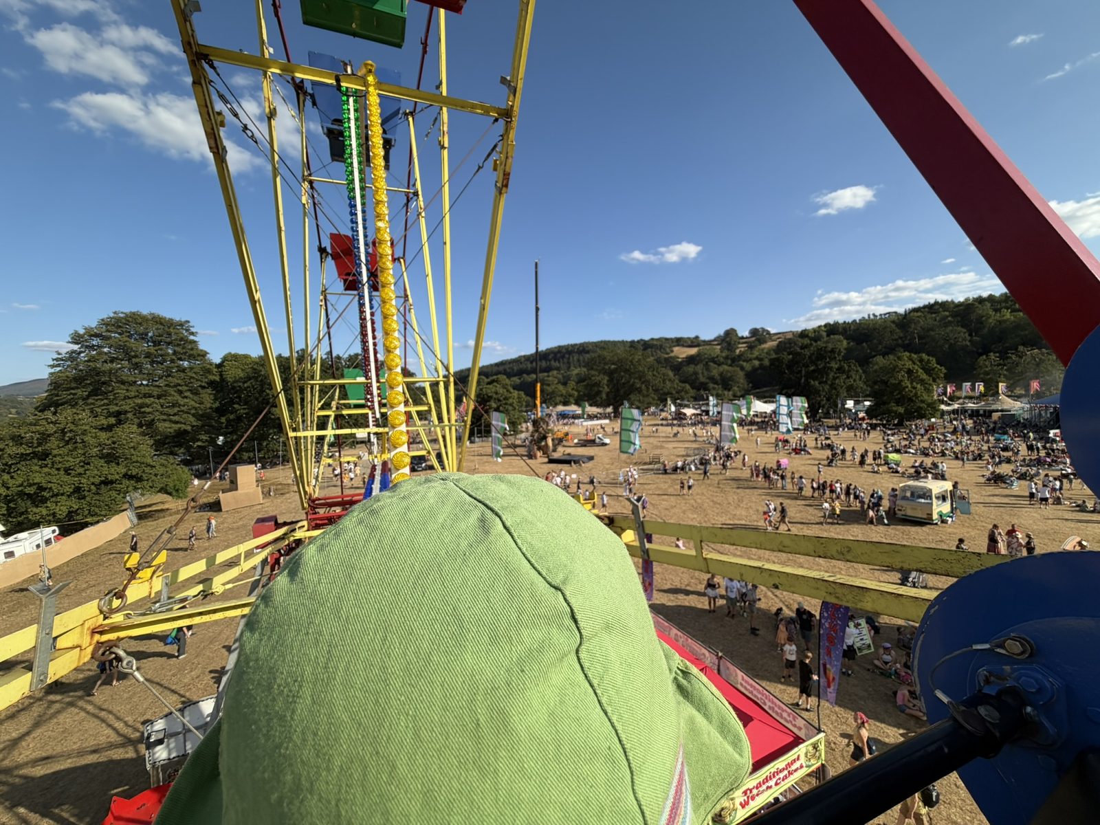 Looking out from the top of the Ferris wheel over the festival field, crowds and stalls below and the wooded hills of the valley beyond
