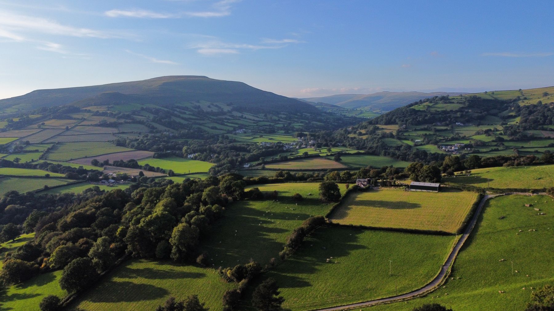 Golden-hour drone view from the cottage: Llanbedr village in the distance, framed by Table Mountain and Pen Cerrig-calch on the left, with Little Pengilfach in the foreground