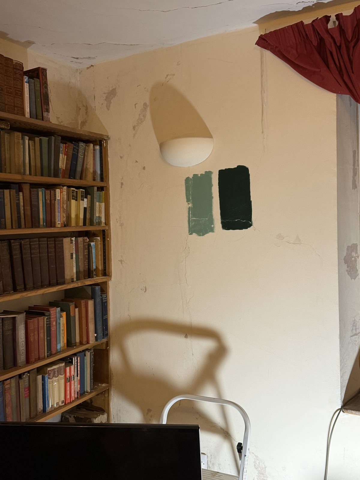 Two test patches of green paint brushed onto a freshly plastered sitting-room wall, beside an old bookcase
