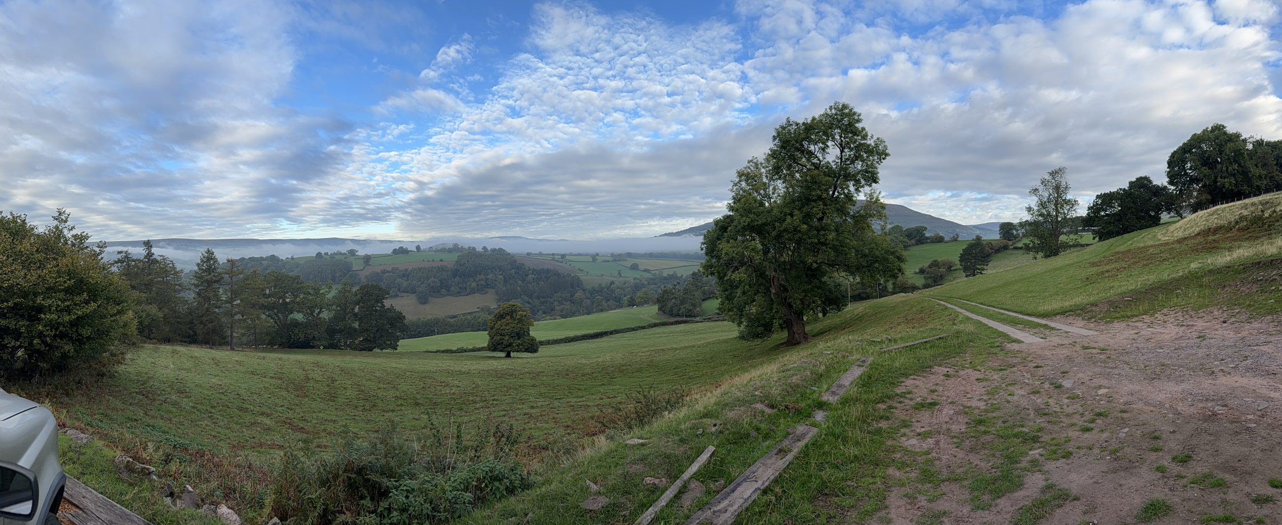 A wide panorama of the valley in September, the fields green again after the rain, hills and woodland under a soft, cloudy autumn sky