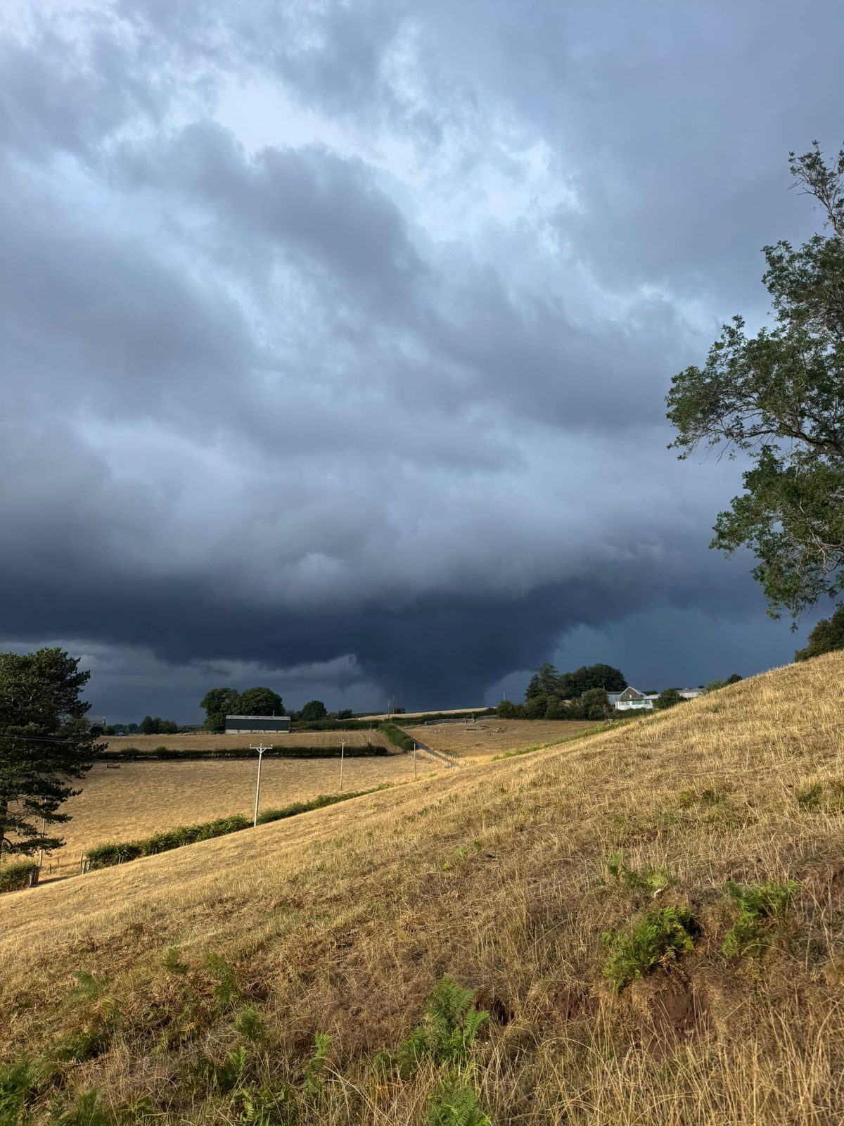 Dark storm clouds gathering over the parched fields and hedgerows of the valley, rain on its way