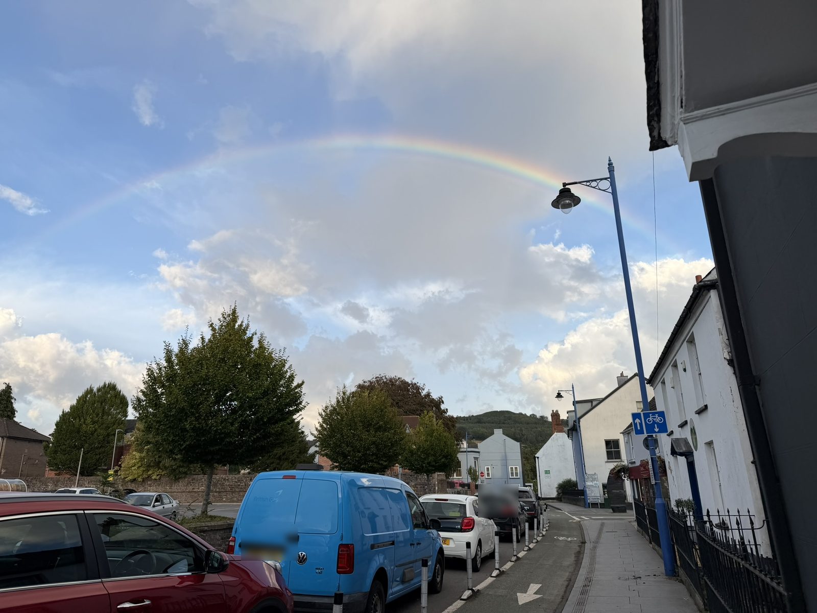 A bright rainbow arcing over a street in Abergavenny after the rain, with houses, a street lamp and the hills beyond