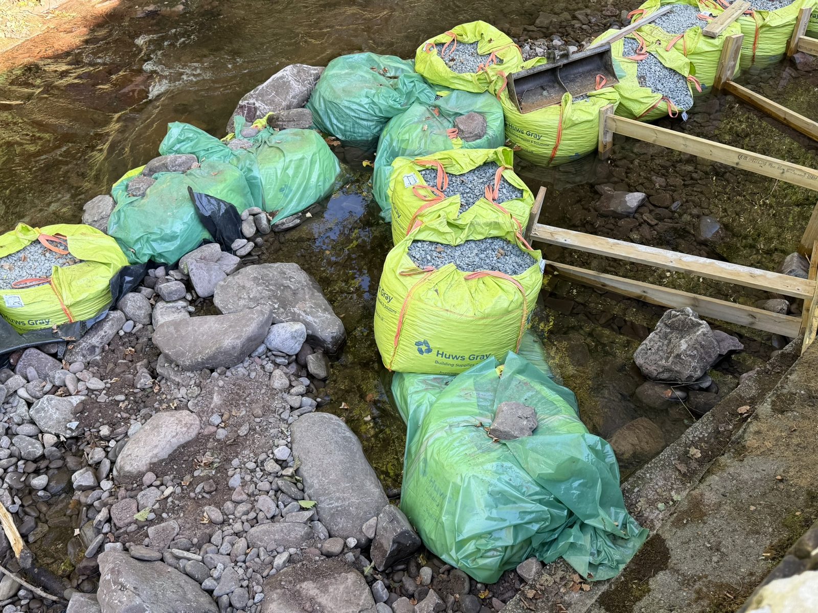 Rows of large gravel-filled bags and timber shuttering set into the river to repair the stone retaining walls