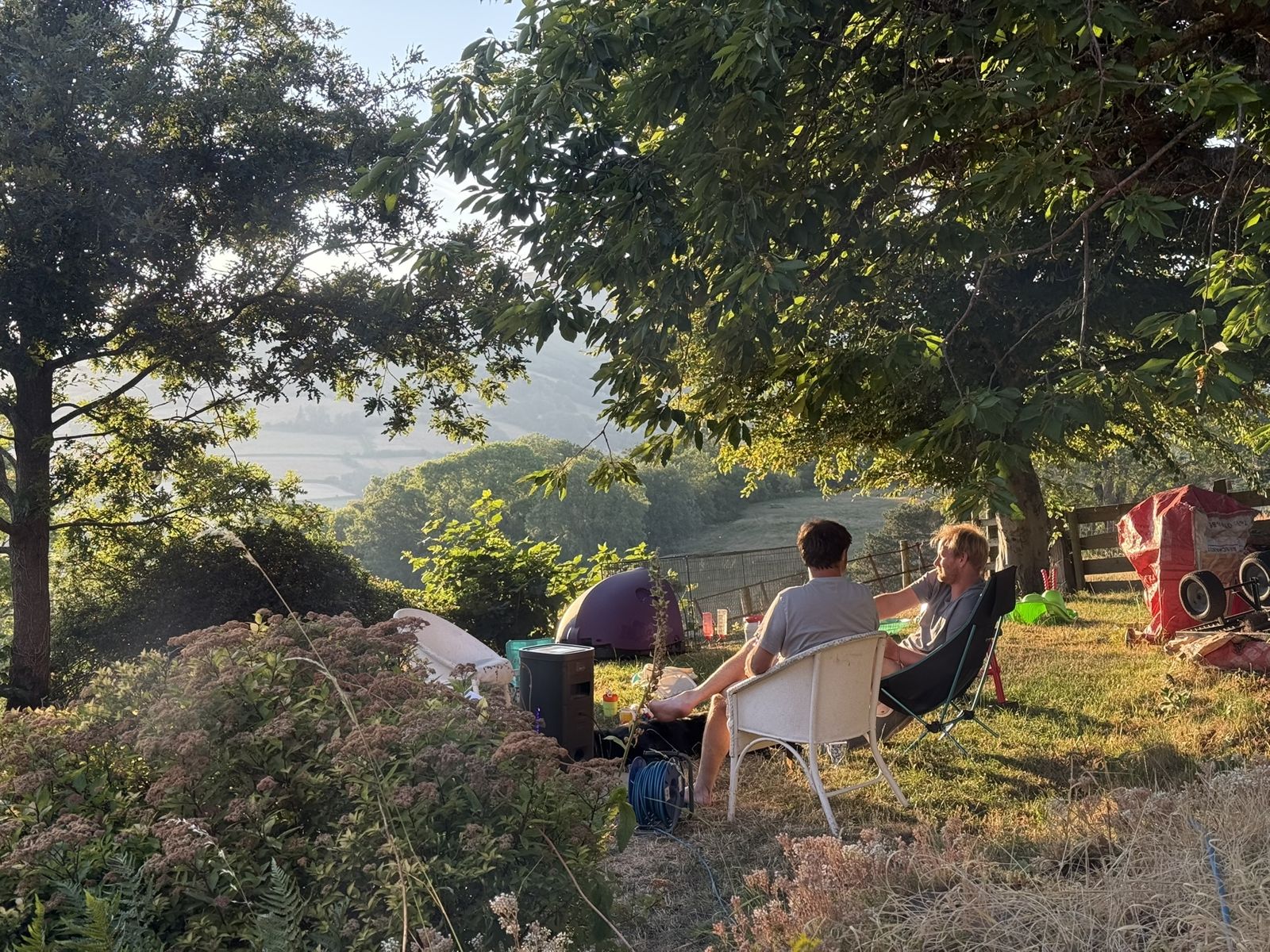 Ewan and Tom Jayne relaxing on Ted's Lawn in the evening sun beside the cottages, July 2026